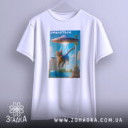 Футболка гумор НЛО, біла, підвішена на вішалці, фон нейтральний, принт з котом, що летить під космічним кораблем, яскраві кольори, деталі фону включають архітектурні елементи.