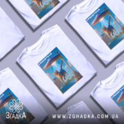 Футболка гумор НЛО, біла, зображена на манекені, фон нейтральний, принт з котом, що летить під космічним кораблем, яскраві кольори, деталі фону включають архітектурні елементи.