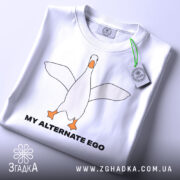 Футболка гусак альтер его, біла, зображена з верхнього ракурсу, на фоні світло-сірого кольору, принт з гусаком в центрі, текст 'MY ALTERNATE EGO' чорного кольору, на футболці є етикетка з зеленим шнурком.