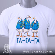 Футболка гуси га га га біла, зображення трьох гусей у синіх худі, лежить на поверхні, принт чіткий, текст "ГА-ГА-ГА" під ними, на футболці є етикетка з зеленим шнурком.