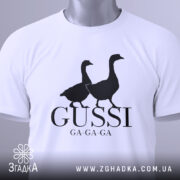 Футболка гуси мем, біла, згорнута, верхній ракурс, фон світло-сірий, принт з двома чорними гусями та написом 'GUSSI GA-GA-GA', з етикеткою зеленого кольору.