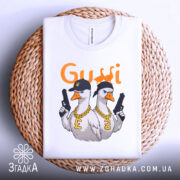 Футболка гуси в кепках білого кольору, складена на плетеній кошику, фон світло-сірий, принт з двома гусями в кепках та золотими ланцюгами, один гусак тримає пістолет.