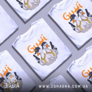 Футболка гуси в кепках білого кольору, зображена на манекені з правого ракурсу, фон світло-сірий, принт з двома гусями в кепках та золотими ланцюгами, один гусак тримає пістолет.