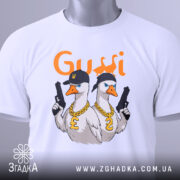 Футболка гуси в кепках білого кольору, складена на поверхні, з видимим етикеткою, фон світло-сірий, принт з двома гусями в кепках та золотими ланцюгами, один гусак тримає пістолет.