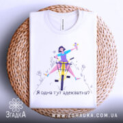 Футболка я адекватна, білого кольору, зображена в складеному вигляді на плетеній основі, принт з дівчиною на велосипеді, яка тримає квіти, текст під малюнком: 'Я одна тут адекватна?'.