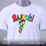 Футболка я алкаш. Біла футболка, складена на столі, з принтом, що зображує персонажа в зеленій футболці та жовтих шортах, який стрибає з написом 'ЯЛКАШ' кольоровими літерами. На футболці видно етикетку.