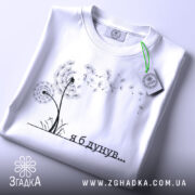 Футболка я б дунув, білого кольору, складена на поверхні, фон світло-сірий, принт з дикими квітами та написом чорного кольору, на комірці є етикетка з зеленим шнурком.