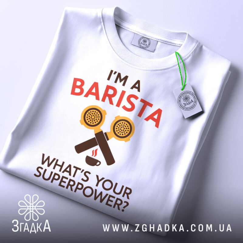 Футболка я бариста, біла, зображена з верхнього ракурсу, фон світлий, принт аналогічний попередньому, на футболці є етикетка з зеленим шнурком.