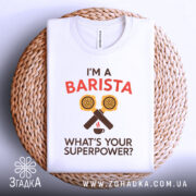 Футболка я бариста, біла, зображена зверху на плетеній підставці, фон світлий, принт аналогічний попереднім, футболка складена акуратно.
