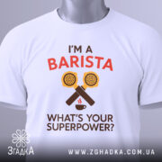 Футболка я бариста, біла, зображена з верхнього ракурсу, фон світлий, принт аналогічний попередньому, на футболці є етикетка з зеленим шнурком.