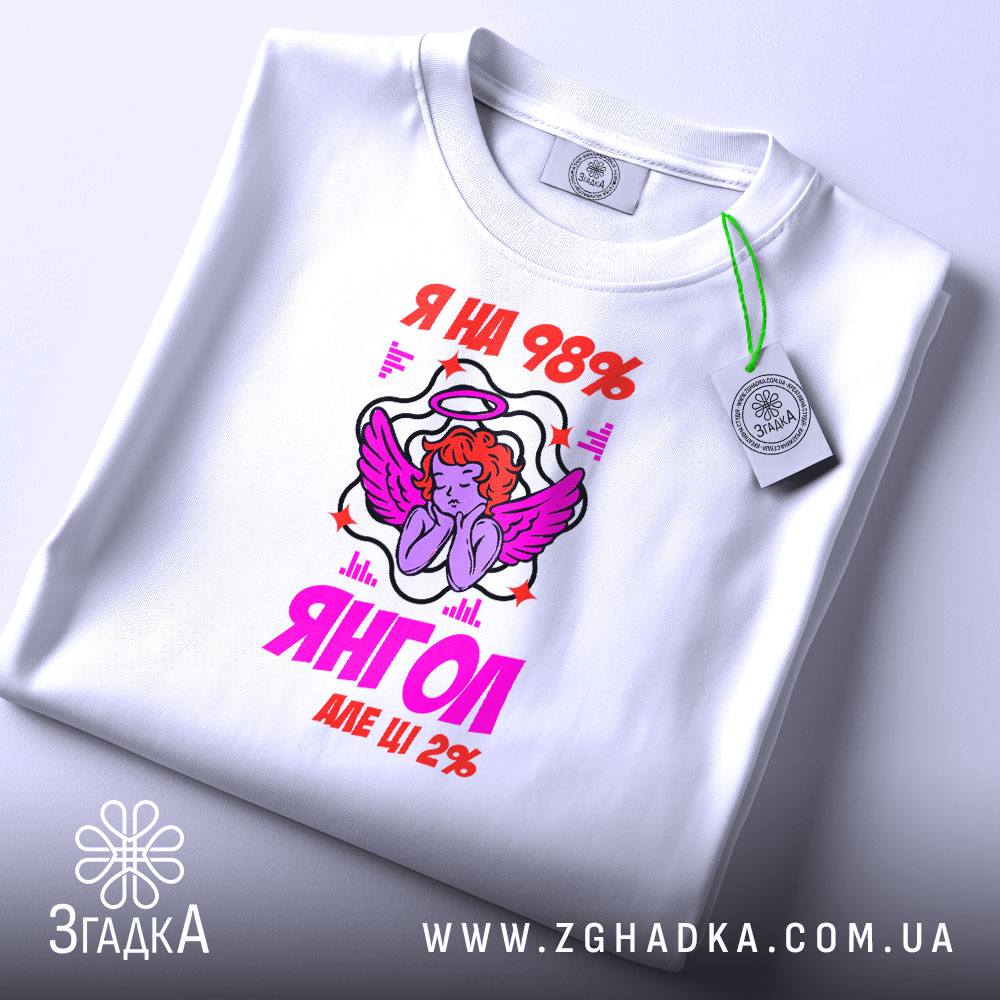 Футболка я янгол, біла, складена на поверхні, фон світлий, принт з ангелом та написом 'Я на 98% янгол, але ще 2%', присутня етикетка з зеленим шнурком.