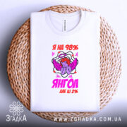 Футболка я янгол, біла, складена на плетеній основі, фон світлий, принт з ангелом та написом 'Я на 98% янгол, але ще 2%', етикетка видима.