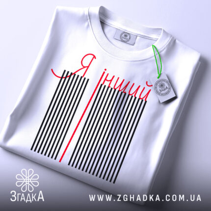 Футболка я інший. Біла футболка, складена на плоскій поверхні, з видимим етикеткою. На футболці чорні вертикальні смуги з червоною написом 'Я інший'. Фон світло-сірий.