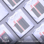 Футболка я інший. Біла футболка з коротким рукавом, зображена з правого ракурсу на манекені. На футболці чорні вертикальні смуги з червоною написом 'Я інший'. Фон світло-сірий.