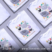 Футболка я керую цими курочками. Біла футболка з коротким рукавом, зображена з фронтального ракурсу на манекені. На фоні світло-сірий колір. Принт містить малюнки курей та квітів, виконаний у яскравих кольорах, з текстом внизу.