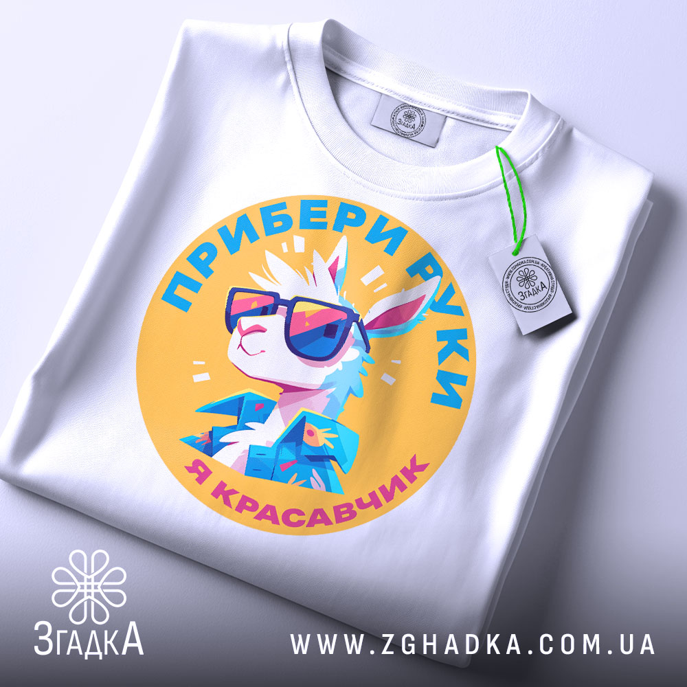 Футболка я красавчик, біла, зображена зверху, на фоні світло-сірого кольору, принт з мультяшним кроликом у сонцезахисних окулярах, текст українською мовою, на етикетці зелена стрічка.
