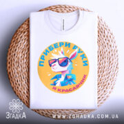 Футболка я красавчик, біла, зображена зверху на плетеній основі, фон світло-сірий, принт з мультяшним кроликом у сонцезахисних окулярах, текст українською мовою.