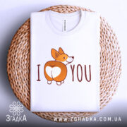 Футболка я люблю білого кольору, зображена в плоскому вигляді на плетеній основі, фон білий, принт з коргі, що показує свою попу, з написом 'I ♥ YOU', на комірці видно етикетку.