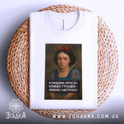 Футболка я людина проста. Біла футболка, складена на плетеній основі, з принтом в центрі. Принт з дівчиною та текстом чорного кольору під зображенням. Фон нейтральний, створює контраст з футболкою.