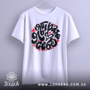 Футболка я обираю себе. Біла футболка, підвішена на вішалці, з коротким рукавом і яскравим принтом чорного кольору з червоними сердечками. Фон світло-сірий, що акцентує увагу на дизайні.