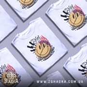 Футболка я окей. Біла футболка з принтом, на якому зображено усміхнене обличчя з фіолетовим волоссям та блискавками, знята з фронтального ракурсу на нейтральному фоні.