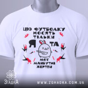 Футболка я та жертви, біла, зображена зверху, на фоні світло-сірого градієнту, принт з малюнком кролика та текстом, на футболці є етикетка з зеленим шнурком.