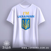 Футболка я українець англійською, біла, зображена на вішалці, фон світло-сірий, принт містить текст 'I'M UKRAINIAN' жовтого та синього кольорів, а також герб України.