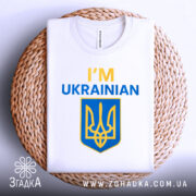 Футболка я українець англійською, біла, зображена зверху, складена на плетеній кошику, фон світлий, принт містить текст 'I'M UKRAINIAN' жовтого та синього кольорів, а також герб України.