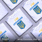 Футболка я українець англійською, біла, зображена з фронтального ракурсу на манекені, фон нейтральний, принт містить текст 'I'M UKRAINIAN' жовтого та синього кольорів, а також герб України.