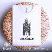 Футболка я українець, білого кольору, складена на кошику, зображена з верхнього ракурсу, фон світло-сірий, принт чорного кольору з написом 'I'M UKRAINIAN'.