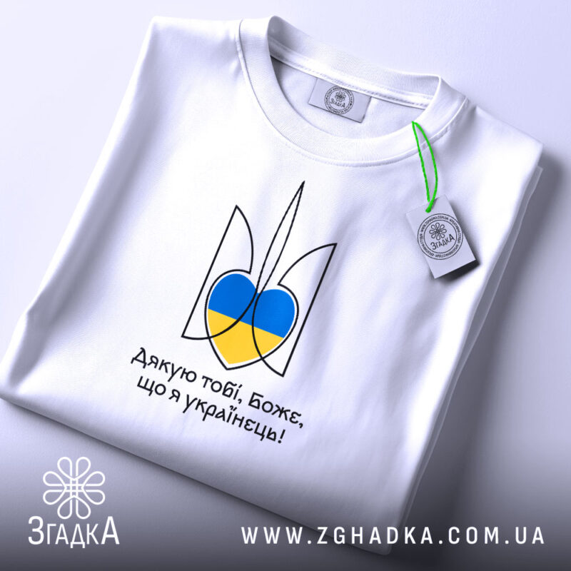 Футболка я українець, біла, зображена зверху, фон світло-сірий, принт у вигляді тризуба з синьо-жовтими елементами, на футболці також видно етикетку з зеленим шнурком.