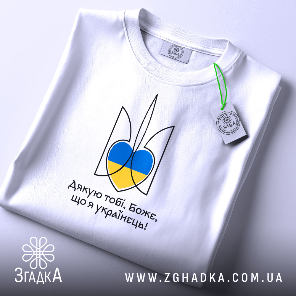 Футболка я українець, біла, зображена зверху, фон світло-сірий, принт у вигляді тризуба з синьо-жовтими елементами, на футболці також видно етикетку з зеленим шнурком.