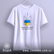 Футболка я українець, біла, зображена з переднього ракурсу, фон світло-сірий, принт у вигляді тризуба з синьо-жовтими елементами та написом 'Дякую тобі, Боже, що я українець!'.