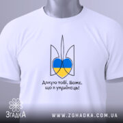 Футболка я українець, біла, зображена зверху, фон світло-сірий, принт у вигляді тризуба з синьо-жовтими елементами, на футболці також видно етикетку з зеленим шнурком.