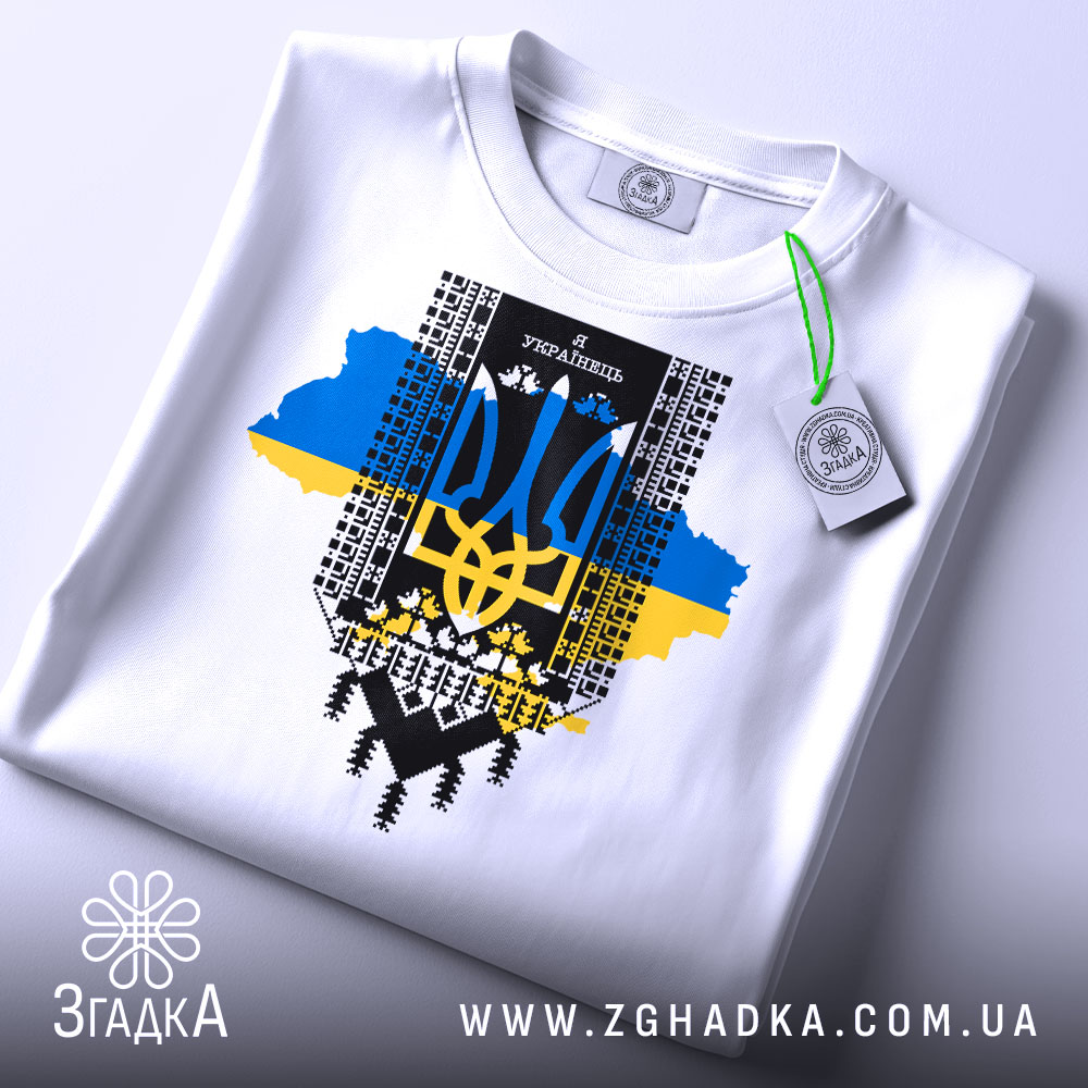 Футболка я українець, біла, складена на поверхні, фон світлий, принт з тризубом, сині та жовті кольори, прикріплена етикетка.