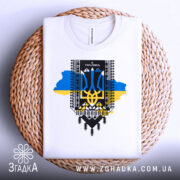 Футболка я українець, біла, складена на плетеній кошику, фон світлий, принт з тризубом, сині та жовті кольори, текст "Я УКРАЇНЕЦЬ".