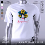 Футболка я українка, білого кольору, зображена на манекені, фон світло-сірий, принт з дівчиною з квітами в волоссі, текст "Я українка!" червоним кольором.