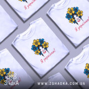 Футболка я українка, білого кольору, зображена на манекені, фон світло-сірий, принт з дівчиною з квітами в волоссі, текст "Я українка!" червоним кольором.