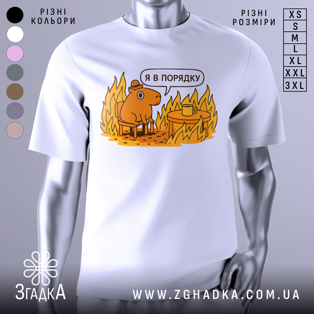 Futbolka Ia V Poriadku Idealnyi Mem Nastrii 1 Футболка я в порядку. Біла футболка на манекені, з принтом, що зображує коричневу тварину на стільці біля столу з чашкою, на фоні полум'я. Принт яскравий, з жовтими та оранжевими відтінками.