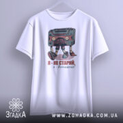 Футболка я вінтажний, білого кольору, підвішена на вішалці, фон світло-сірий, принт з касетою та написом "Я - не старий, я - вінтажний!" у кольорах червоного та зеленого.