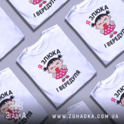 Футболка я злюка вередуля. Біла футболка з коротким рукавом, зображення дівчинки в рожевій сукні з горошками, яка показує язика. Принт розташований на грудях, фон світло-сірий.