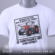 Футболка як танкіст тракторист, біла, зображена з верхнього ракурсу, фон світлий, принт з червоним трактором та текстом, з етикеткою зеленого кольору.