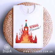 Футболка як воно палає, біла, складена на плетеній основі, фон білий, принт з червоними і жовтими вогнями, зображення Кремля з годинником і зіркою.