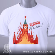 Футболка як воно палає, біла, складена на поверхні, фон світло-сірий, принт з червоними і жовтими вогнями, зображення Кремля з годинником і зіркою, на футболці є етикетка з зеленим шнурком.