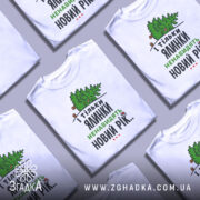 Футболка ялинки новий рік, біла, зображена на манекені з правого боку, фон нейтральний, принт з ялинкою та текстом у зеленому та чорному кольорах.