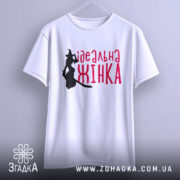 Футболка ідеальна жінка, біла, підвішена на вішалці, фон світло-сірий, принт з силуетом відьми та написом червоним шрифтом 'ідеальна жінка'.