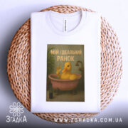 Футболка ідеальний ранок, біла, зображена зверху на плетеній основі, фон нейтральний, принт з жовтою качкою у ванні, текст 'МІЙ ІДЕАЛЬНИЙ РАНОК'.