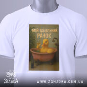 Футболка ідеальний ранок, біла, зображена зверху, фон світлий, принт з жовтою качкою у ванні, текст 'МІЙ ІДЕАЛЬНИЙ РАНОК', на комірці видна етикетка.