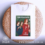 Футболка йди працювати, біла, лежить на плетеному кошику, фон світло-сірий, принт з жінками в традиційному одязі, червона сукня, зелений фон з рослинністю, текст "ЙДИ ПРАЦЮВАТИ, ЦЕ ТРАВЛЯ", видно етикетку.