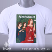 Футболка йди працювати, біла, лежить на столі, фон світло-сірий, принт з жінками в традиційному одязі, червона сукня, зелений фон з рослинністю, текст "ЙДИ ПРАЦЮВАТИ, ЦЕ ТРАВЛЯ", на футболці є етикетка з зеленим шнурком.